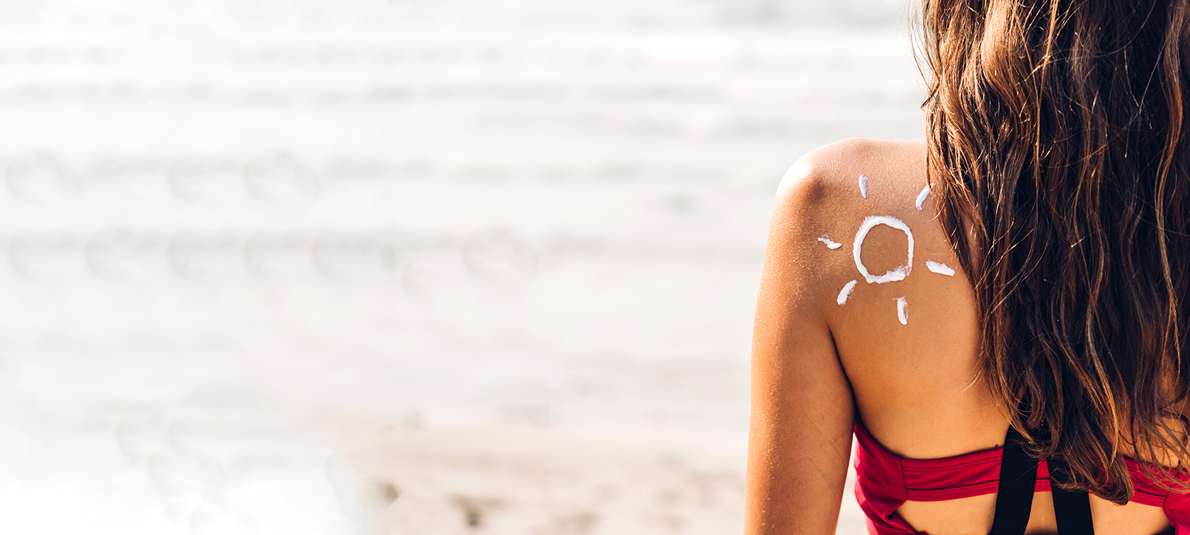 Frau mit einer Sonne aus Sonnencreme, auf der Schulter, am Strand.