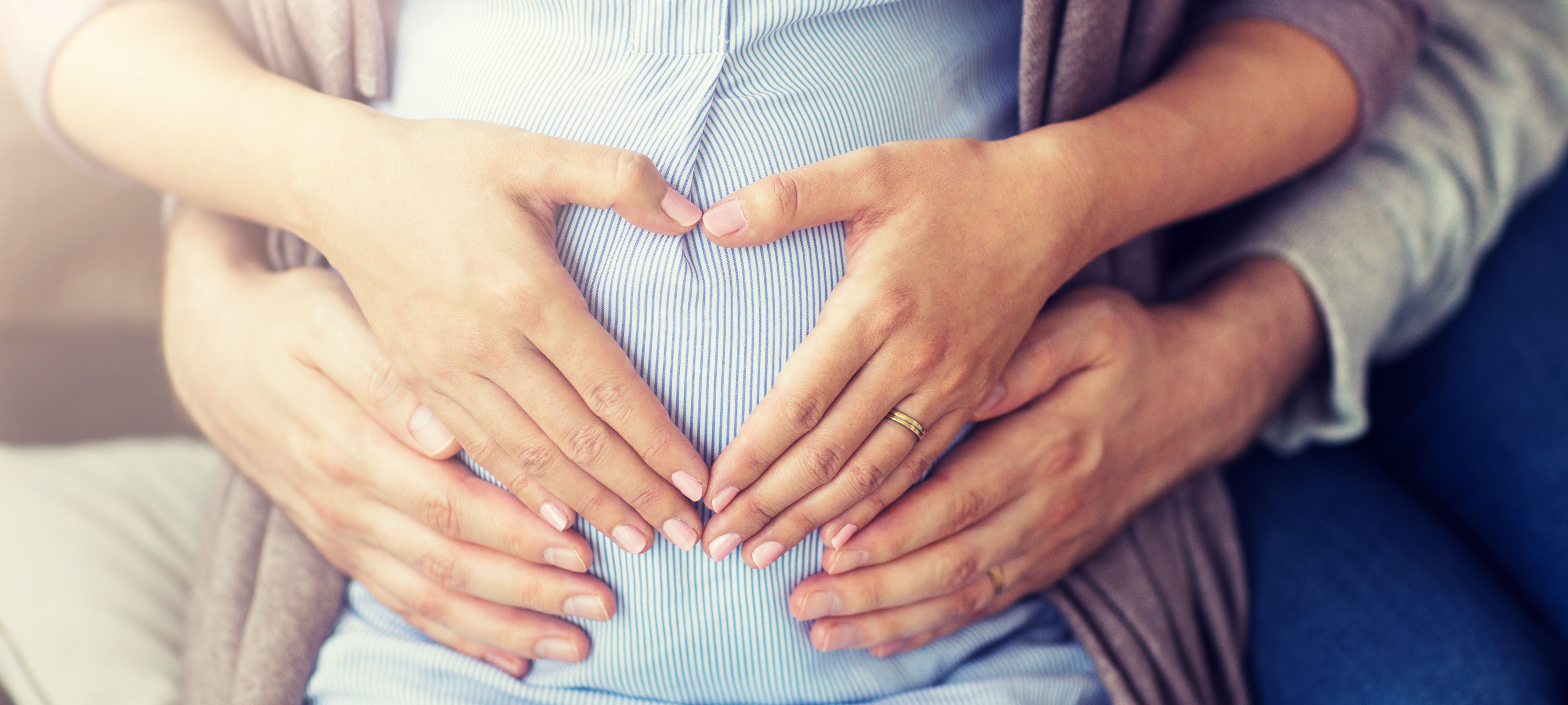 Nahaufname einer Frau mit Haenden zu einem Herz formend auf dem schwangeren Bauch Nahaufname einer Frau mit Haenden zu einem Herz formend auf dem schwangeren Bauch