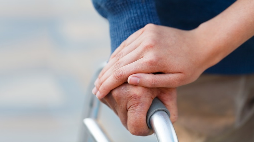 Hand einer Pflegerin liegt sanft auf der Hand eines älteren Mannes mit Gehhilfe Hand einer Pflegerin liegt sanft auf der Hand eines älteren Mannes mit Gehhilfe