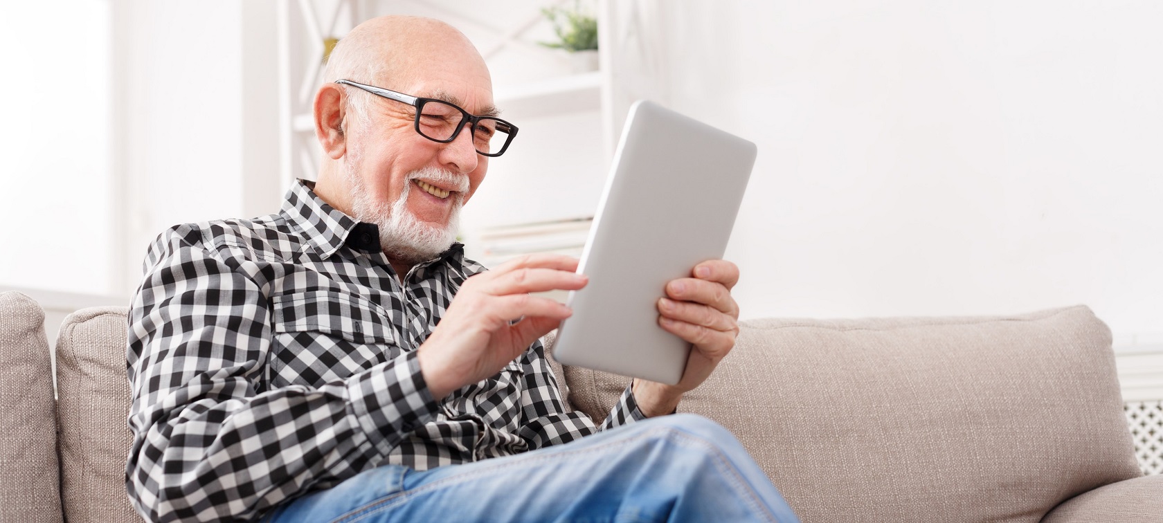 Senior liest freudig Nachrichten auf seinem Tablet im Wohnzimmer Senior liest freudig Nachrichten auf seinem Tablet im Wohnzimmer