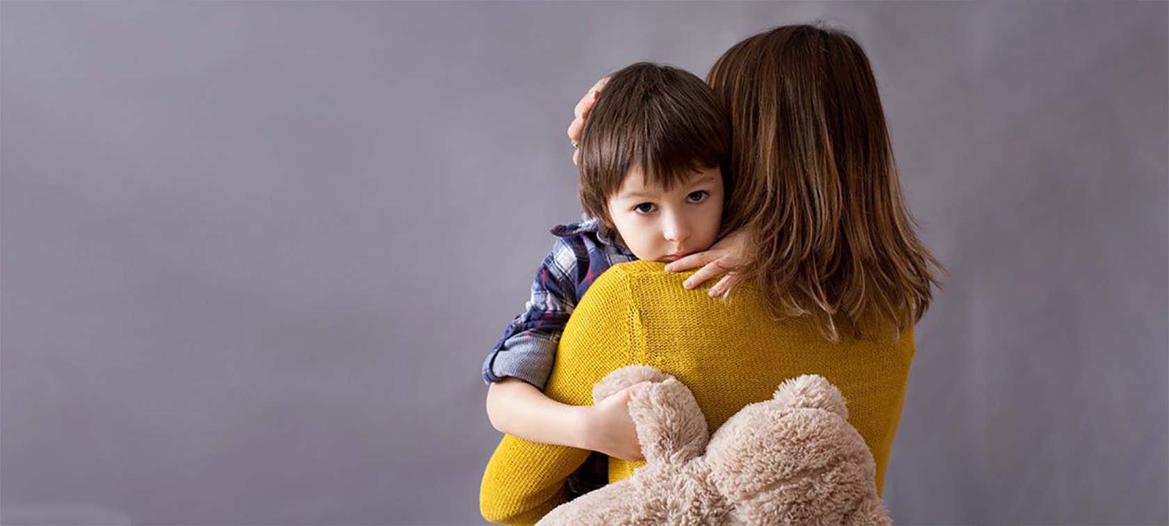 Mutter hat ihren Sohn auf dem Arm, der mit traurigem Gesicht in die Kamera sieht und seinen Teddy festhält Mutter hat ihren Sohn auf dem Arm, der mit traurigem Gesicht in die Kamera sieht und seinen Teddy festhält