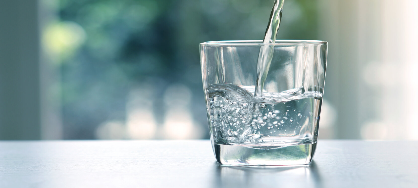 Glas Wasser in das von oben Wasser weiter eingegossen wird. Glas Wasser in das von oben Wasser weiter eingegossen wird.